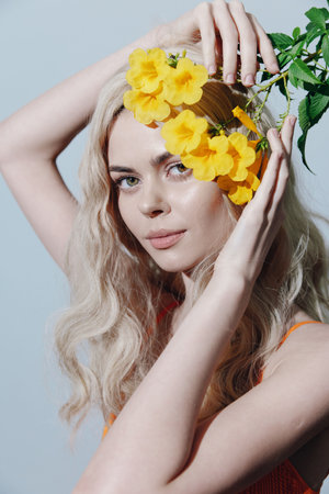 Delicate beauty portrait of a young woman with long blonde hair holding vibrant yellow flowers, capturing a serene and joyful expression against a soft backdrop.の写真素材