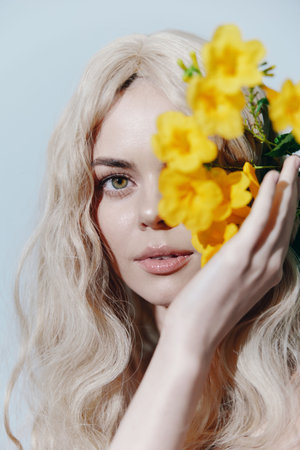 Blonde woman with flowers, showcasing beauty and emotions in a soft light setting, perfect for beauty and fashion themes.の写真素材