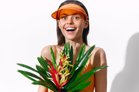 Joyful model in orange attire holding tropical flowers, showcasing vibrant emotions and summer freshness.の写真素材