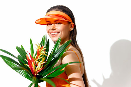 Cheerful young woman in bright orange outfit with flower bouquet, showcasing vibrant tropical style and joyful emotions against a clean white background.の写真素材