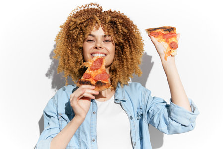 Happy young African American woman with curly hair holding slices of pizza, showcasing joy and love for food, perfect for concepts like healthy eating and indulgenceの写真素材