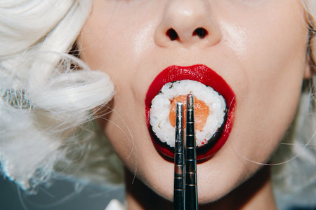 Bold and vibrant close-up of a woman with bright red lips holding sushi with chopsticks, showcasing...