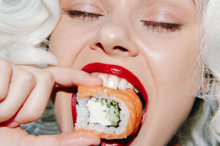 Stylish woman with blonde hair enjoying sushi, showcasing vibrant emotions and bold colors, perfect for food photography and lifestyle concepts.の写真素材