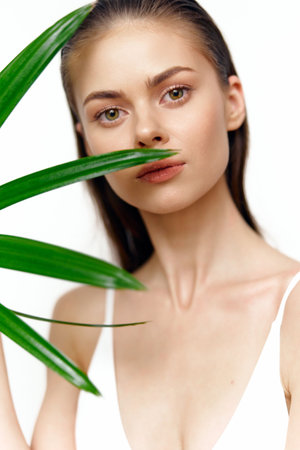 Natural beauty portrait of a young woman with green plant, showcasing serene expression and minimalist aesthetics against a white background.の写真素材
