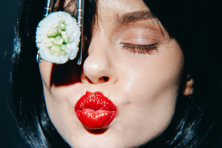 Stylish woman with red lips pursing her lips while holding sushi, showcasing an elegant fusion of food and fashion in vibrant colors.の写真素材