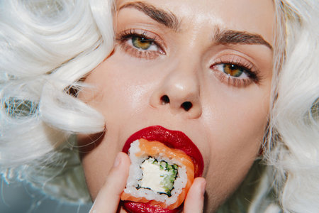 Woman with white curls and red lips eating sushi close-up, showcasing vibrant colors, modern style, and a playful atmosphere in a food concept.の写真素材