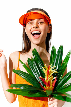 Cheerful young woman in vibrant orange outfit holding tropical leaves, showcasing joy and summer vibes in a bright, colorful setting.の写真素材