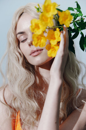 A serene blonde model holds bright yellow flowers, embodying natures beauty in a soft and colorful setting, perfect for seasonal or floral-themed projects.の写真素材