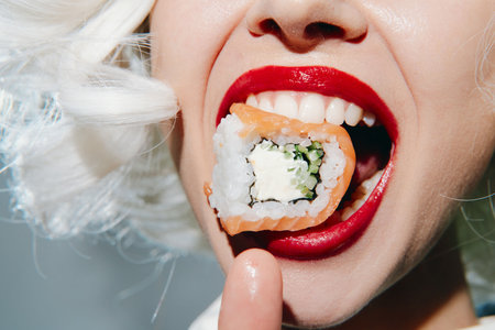 A close-up of a joyful woman with white hair enjoying sushi, showcasing bright red lips and vibrant colors, ideal for food-related themes and culinary art.の写真素材