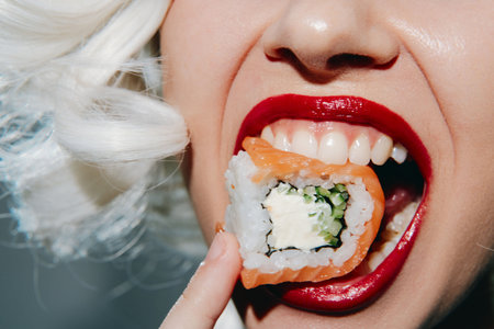 Close-up of a woman with platinum blonde hair enjoying sushi, showcasing vibrant colors and playful emotion in a modern, stylish setting.の写真素材