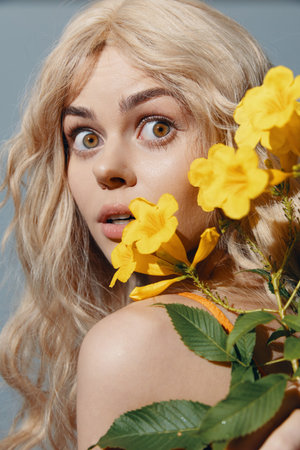 Surprised young woman with blonde hair holding yellow flowers, vibrant colors, expressing joy,...