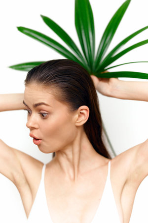 Young woman with long hair expressing surprise, styled with tropical leaves in the background,...