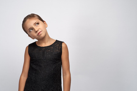 Portrait of pensive pretty girl brunette in a black dress. Beautiful doubtful indecisive child looking up thoughtful eyes, with a puzzled expression thinking something.の写真素材
