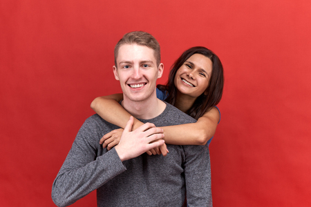 Happy beautiful couple smiling widely at the camera showing white teeth. Lovers hugging in the isolated red background.の写真素材