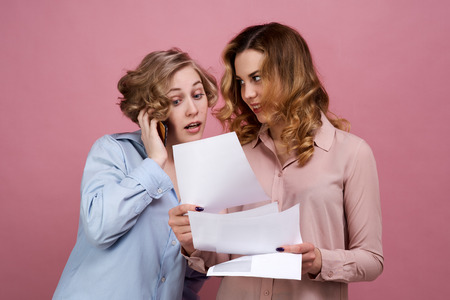 two young girls are holding documents and with satisfied expression discuss result by phone. Unexpected success and fortune raised them up. concept of trading, financial operations, successful examsの写真素材
