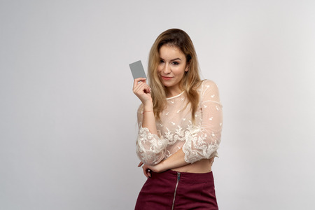 young attractive girl looks impressively at the camera, holding a plastic credit Bank card in front of her hand. Studio portrait on an isolated gray phoneo.の写真素材