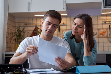 a young couple sitting at a table in the kitchen understands the finances of a young family, studying accounts and tax documents. Serious focused expressionの写真素材