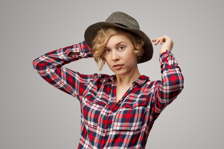 attractive curly blonde in a plaid shirt and cowboy hat looks closely at the camera with a calm neutral expression. Studio portrait on isolated backgroundの写真素材