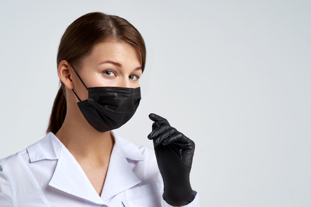 beautiful young doctor woman in protective medical mask and medical black gloves smiling eyes. Studio portrait on isolated backgroundの写真素材