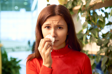 a pretty young girl presses a napkin to her nose. she suffers from allergies and runny nose. concert of health viral infections seasonal allergies.の写真素材