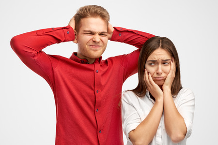 Photo of desperate annoyed people keeps hands on head, holds palms on ears, ignores annoying sound, feels depressed, has many debts and financial crisis, stands over white background in studio.の写真素材