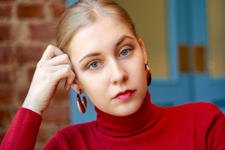 Large portrait of serious girl. A beautiful blonde woman looks intently at the camera, wears a red...