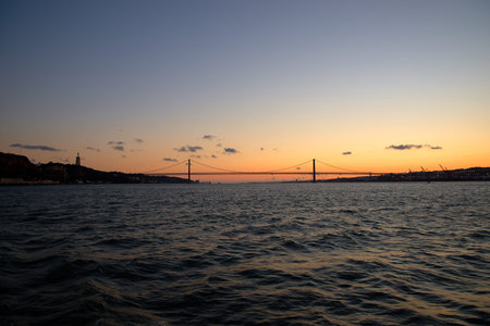 Horizontal photo Bridge April 25-de Abril, connecting Lisbon on North and Almada on the South Bank of Tagus river. Sailing boat in the Tagus River with the Lisbon skyline on the backroundの写真素材