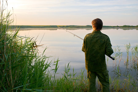 Silhouette of a man fishing. Beautiful picture of a guy at dawn on vacation, holding a fishing rod,...