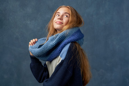 Teenage girl blonde in warm sweater isolated wall