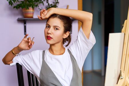 young woman paints picture on an easel at homeの写真素材