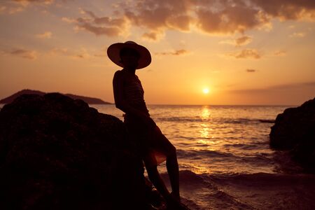 Contrast silhouette of young slender woman against background of Sunny sunset, sea and sandy beach. Warm evening tones. Lady walking on beach in sunset, vacation in city Patong Phuket country Thailandの写真素材