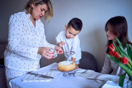 a  family of three, mother, teenage daughter and little son, eating cake in pajamas at a table with tulipsの写真素材