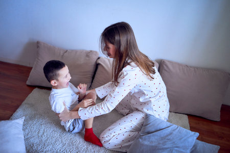 A teenage girl and her little brother are playing and hugging in a pillow fortの写真素材