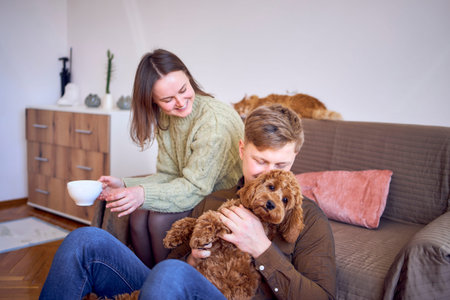 a couple drinking from cups near sofa in living room, red cat sleeping on sofa, cockapoo running...