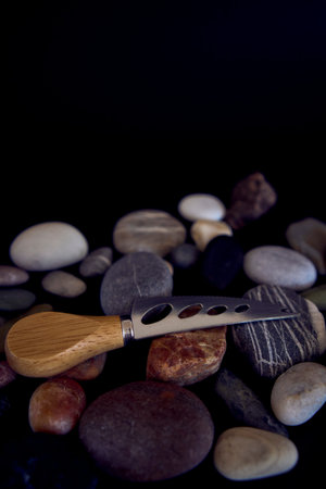 a fish and cheese knife with a wooden handle on a black background with sea pebbles