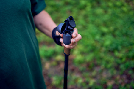 an elderly woman engaged in Nordic walking with sticks in spring forest switches music on headphonesの写真素材
