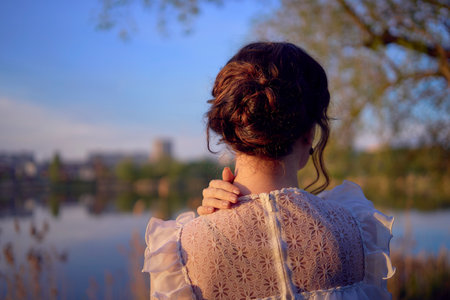 a woman in white vintage dress on the lake shore at sunset hairstyle detailsの写真素材