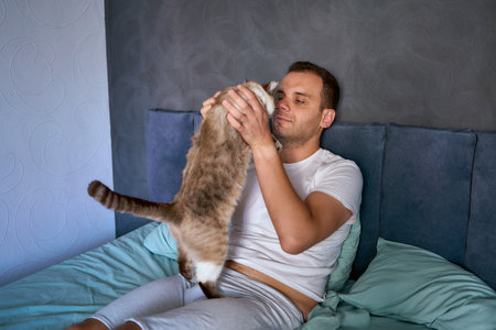 young man pet a cat in bed, morning routine