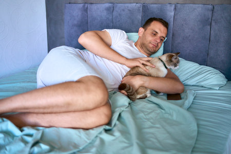 young man pet a cat in bed, morning routineの写真素材