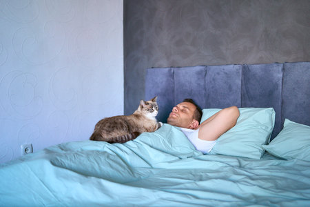 young man sleeping with a cat on his chest, morning routineの写真素材