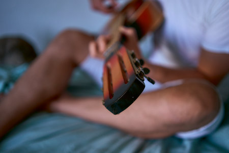 young man is learning to play the guitar at home, a cat is lying next to him and listeningの写真素材