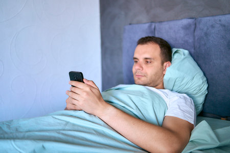 young man scrolls in smartphone in the morning after waking up, morning routineの写真素材
