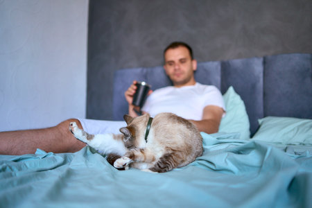 young man drinking morning coffee in bed and scrolling in smartphone, morning routineの写真素材