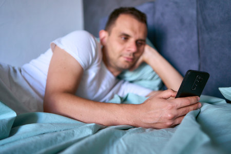 young man scrolls in smartphone in the morning after waking up, morning routineの写真素材