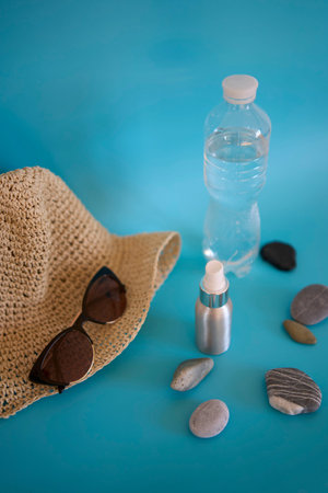 straw hat, sunglasses, bottle of water, sun spray, pebbles on a colored background