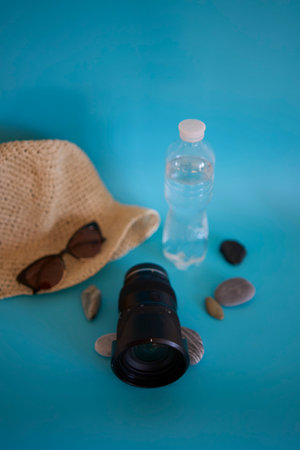 lens, straw hat, sunglasses, bottle of water, sunscreen spray, pebbles on a colored backgroundの写真素材