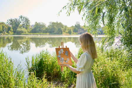 a beautiful young artist in a white dress among the trees on the river bank