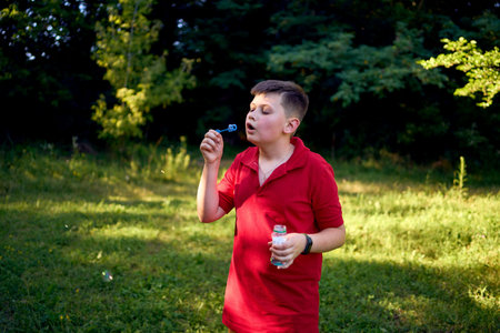 preteen boy in a red T-shirt catches soap bubbles in the park