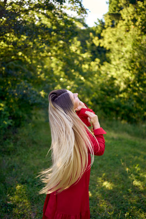 a portrait of a beautiful 30-year-old woman with long blond hair in a red dress in a parkの写真素材