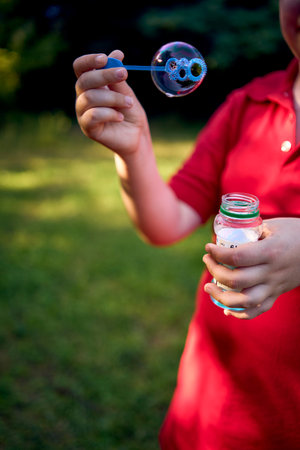 preteen boy in a red T-shirt catches soap bubbles in the park